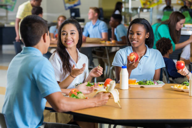 Male and female teenagers enjoy eating lunch together in the school cafeteria. They are wearing school uniforms.